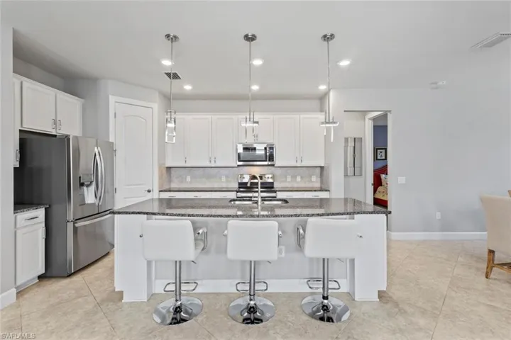 Kitchen featuring dark stone counters, a kitchen bar, hanging light fixtures, stainless steel appliances, and white cabinetry