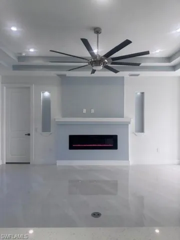 Unfurnished living room with a glass covered fireplace, a ceiling fan, a raised ceiling, and recessed lighting