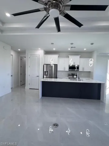 Kitchen with stove, ceiling fan, decorative light fixtures, white cabinetry, and stainless steel refrigerator