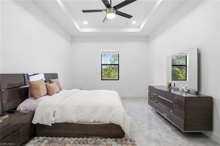 Bedroom with ceiling fan, a raised ceiling, recessed lighting, and light marble finish flooring