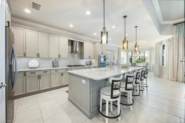 Kitchen with appliances with stainless steel finishes, hanging light fixtures, light stone counters, wall chimney range hood, and a spacious island