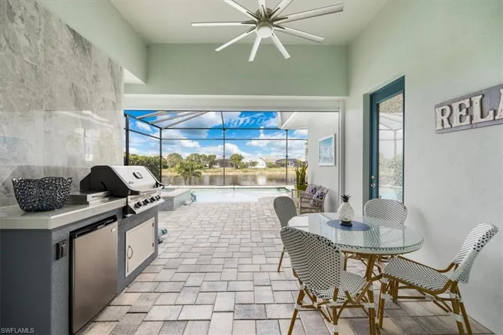 View of patio / terrace featuring a water view, glass enclosure, exterior kitchen, grilling area, and a fenced in pool