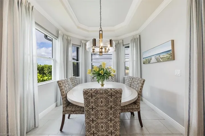 Dining space featuring ornamental molding, light tile patterned flooring, a chandelier, and a raised ceiling