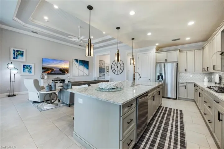Kitchen with a center island with sink, hanging light fixtures, sink, a tray ceiling, and appliances with stainless steel finishes