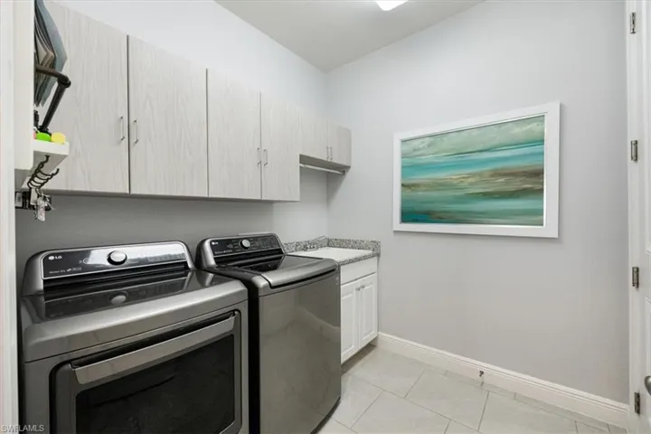 Laundry area featuring sink, light tile patterned flooring, washer and clothes dryer, and cabinets