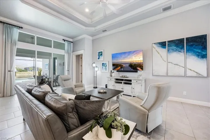 Living room with a high ceiling, ceiling fan, a raised ceiling, crown molding, and light tile patterned floors