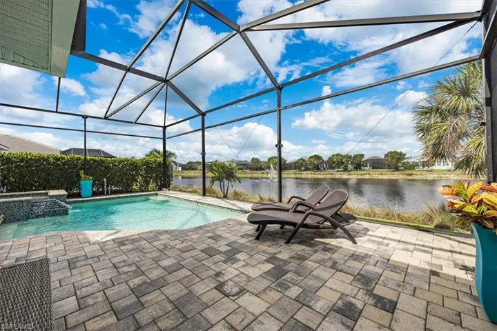 View of swimming pool with an in ground hot tub, a water view, a lanai, and a patio area