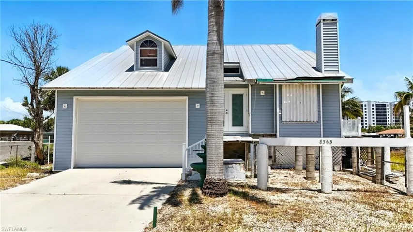 View of front of property featuring driveway, a chimney, a metal roof, and a garage - Virtually Edited Image
