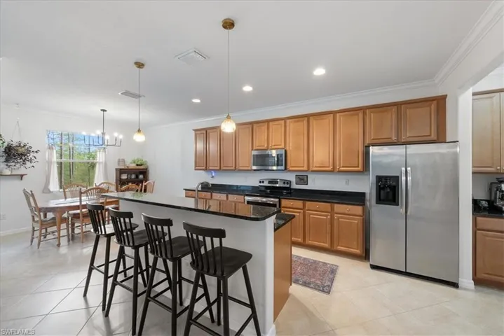 Kitchen featuring stainless steel appliances, ornamental molding, brown cabinetry, a kitchen breakfast bar, and pendant lighting