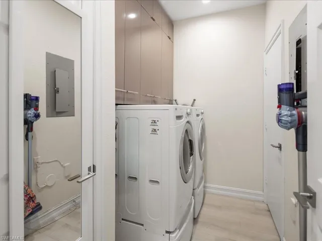 Laundry area with washing machine and dryer, electric panel, and light wood flooring