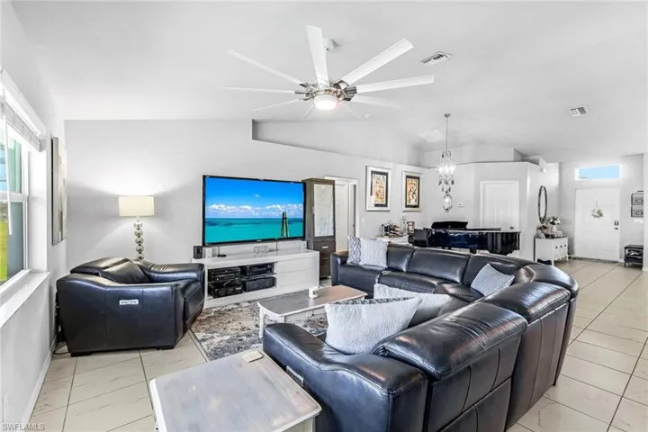 Living room with ceiling fan with notable chandelier, a wealth of natural light, and vaulted ceiling
