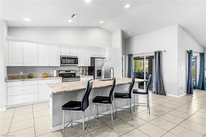 Kitchen with appliances with stainless steel finishes, a kitchen breakfast bar, a center island with sink, and white cabinetry