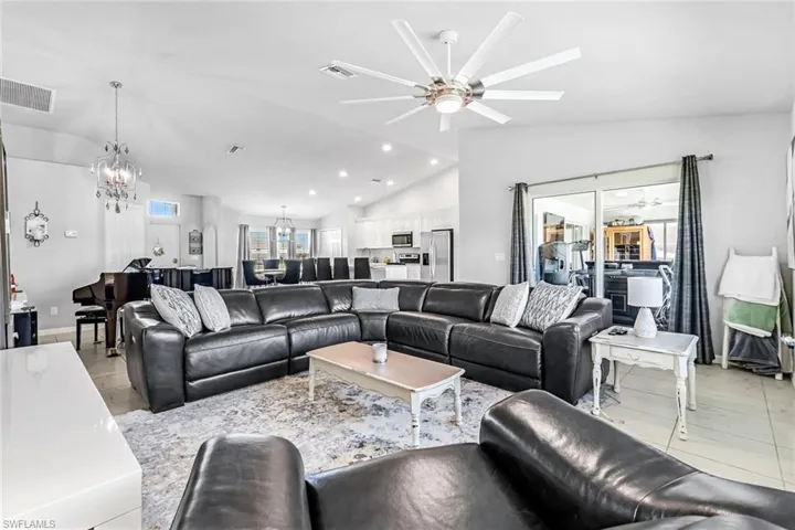 Living room featuring ceiling fan with notable chandelier, lofted ceiling, and light tile patterned flooring