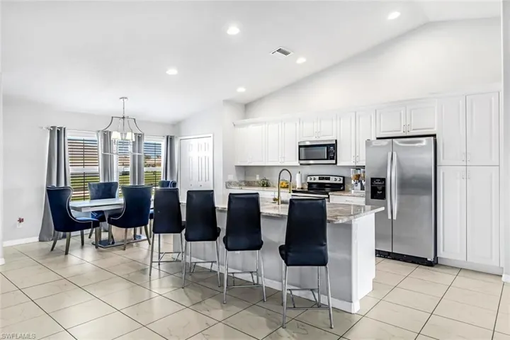 Kitchen featuring vaulted ceiling, a center island with sink, appliances with stainless steel finishes, white cabinetry, and light stone counters