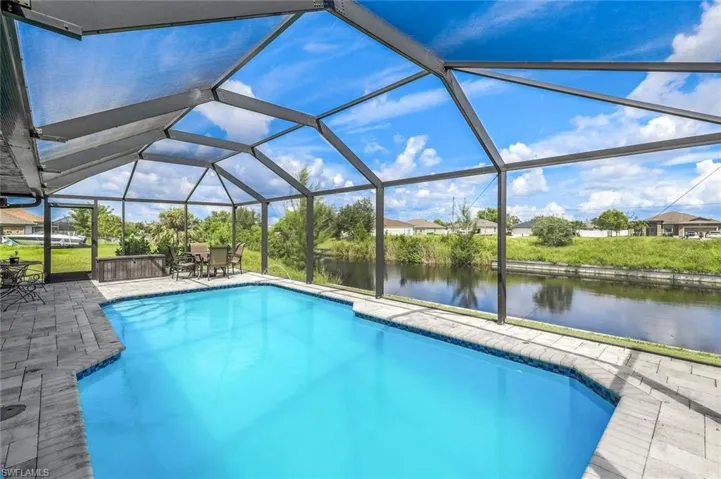 View of pool featuring glass enclosure, a water view, and a patio area