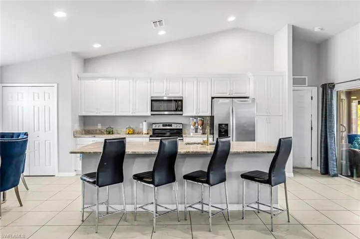 Kitchen with a kitchen island with sink, white cabinetry, stainless steel appliances, and light stone countertops