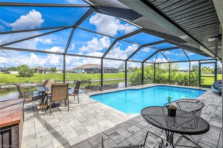 View of pool featuring glass enclosure, a water view, and a patio