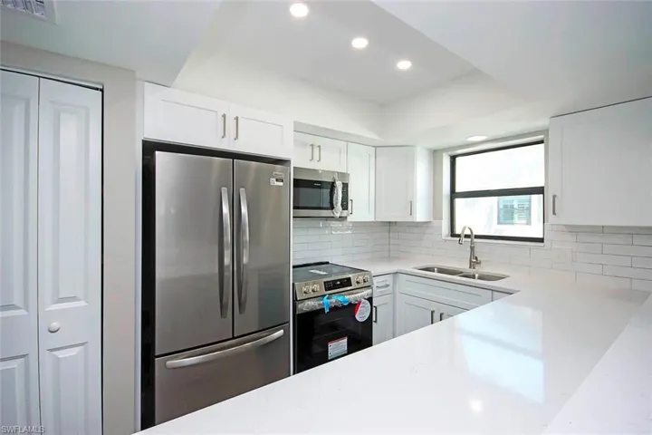 Kitchen featuring new stainless steel appliances, sink, white cabinets, and decorative backsplash