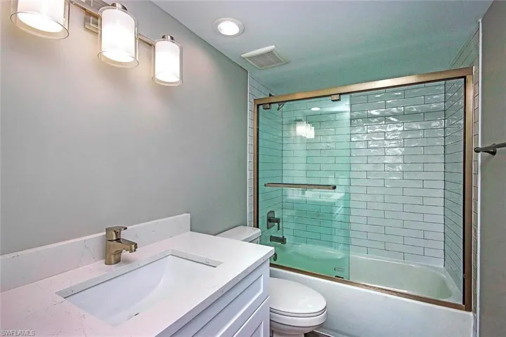 Full bathroom with bath / shower combo with glass door, vanity, and toilet