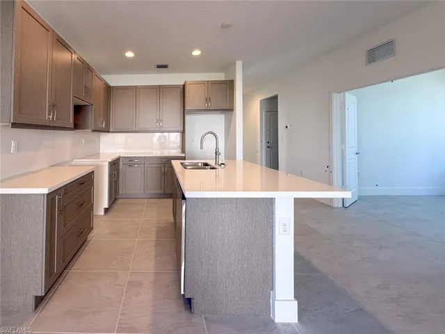 Kitchen with dishwasher, a center island with sink, sink, light tile patterned floors, and a textured ceiling