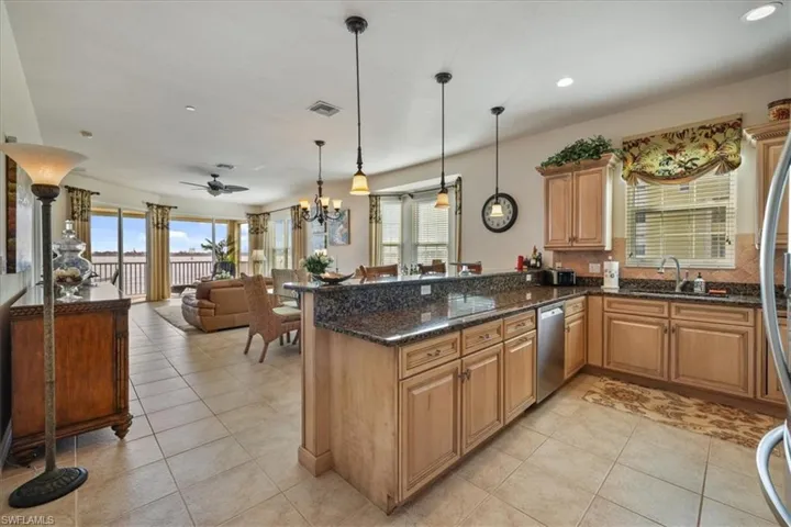 Kitchen featuring light tile patterned flooring, dark stone counters, decorative light fixtures, open floor plan, and a chandelier
