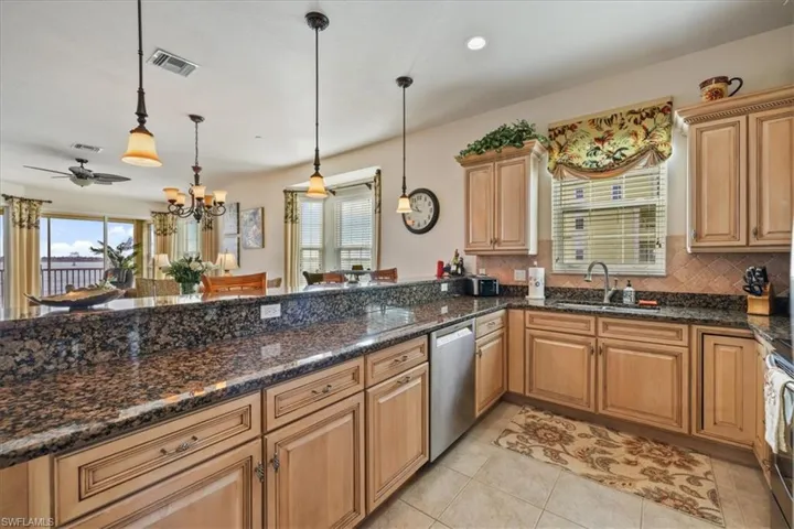 Kitchen featuring backsplash, hanging light fixtures, appliances with stainless steel finishes, light tile patterned floors, and dark stone countertops