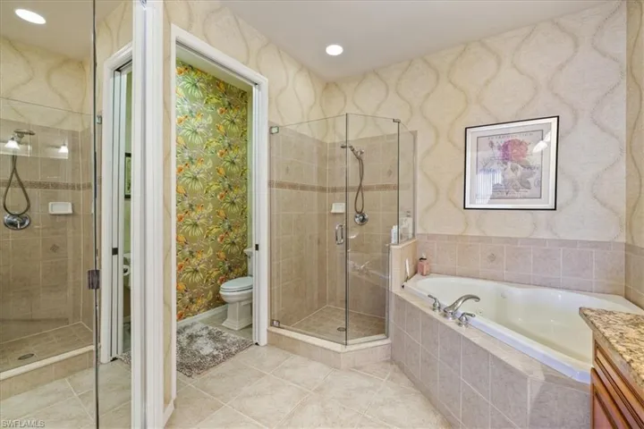 Bathroom featuring wallpapered walls, a shower stall, a garden tub, vanity, and light tile patterned flooring