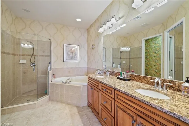 Bathroom featuring double vanity, a stall shower, light tile patterned flooring, a garden tub, and wallpapered walls