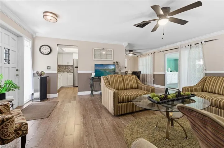 Living area with crown molding, wood-look tile flooring, and ceiling fan