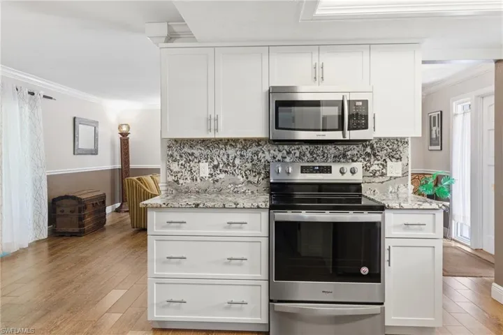 Kitchen with appliances with Granite Counters and Full Granite backsplashes, stainless steel appliances, Floating Shelves, White Shaker Cabinets,  wood-like Tile floors