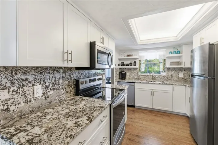 Kitchen with appliances with Granite Counters and Full Granite backsplashes, stainless steel appliances, Floating Shelves, White Shaker Cabinets,  wood-like Tile floors