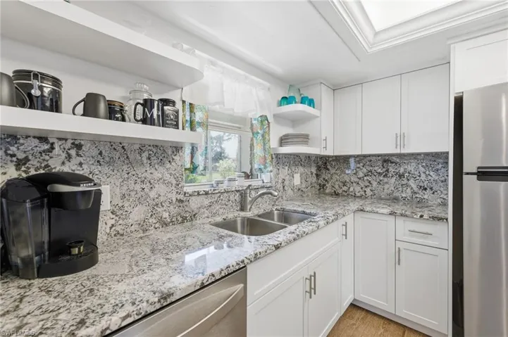 Kitchen with appliances with Granite Counters and Full Granite backsplashes, stainless steel appliances, Floating Shelves, White Shaker Cabinets,  wood-like Tile floors