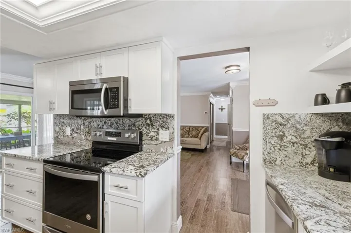 Kitchen with appliances with Granite Counters and Full Granite backsplashes, stainless steel appliances, Floating Shelves, White Shaker Cabinets,  wood-like Tile floors