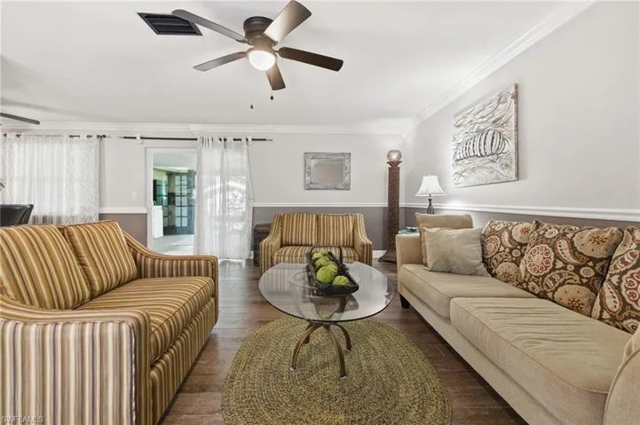 Living area with crown molding, wood-look tile flooring, and ceiling fan