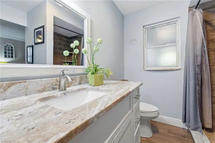 Full bathroom featuring dark wood-like tile flooring, vanity with Granite Countertop, a walk in closet, and a walk-in shower