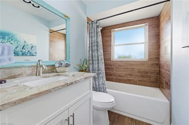 Guest  bath featuring vanity with Granite Counters, shower / bath combination with curtain, and dark wood tile floors