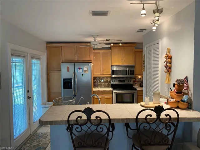 Kitchen featuring appliances with stainless steel finishes, rail lighting, tasteful backsplash, a breakfast bar area, and brown cabinets