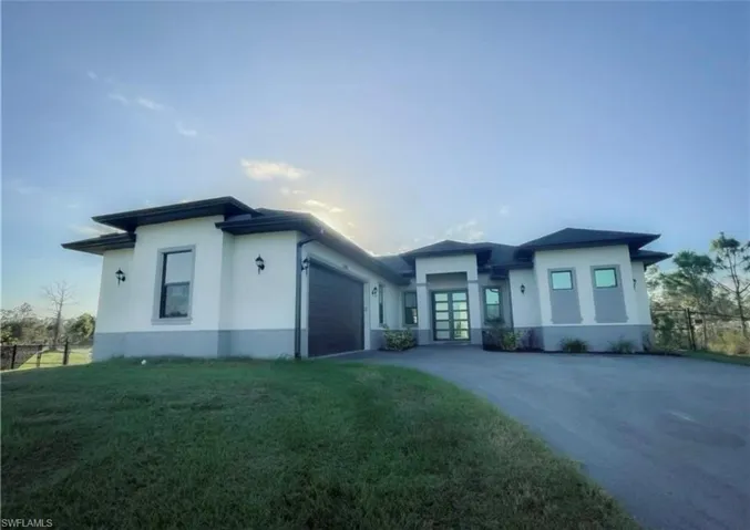 Prairie-style house with fence, concrete driveway, a front yard, stucco siding, and a garage