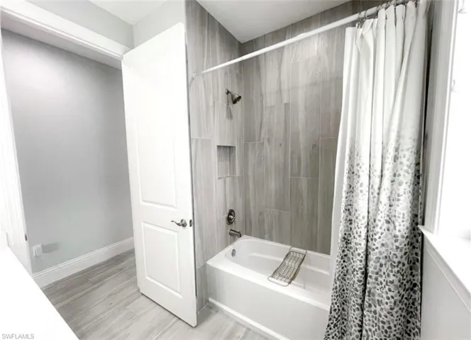 Bathroom featuring shower / tub combo with curtain, baseboards, and wood finished floors
