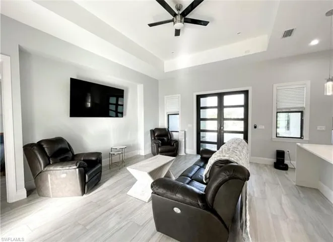 Living area featuring a tray ceiling, a ceiling fan, visible vents, and baseboards