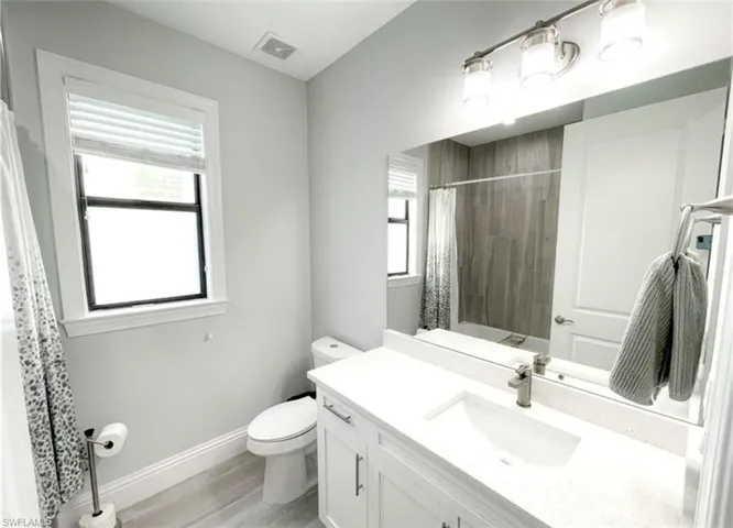 Bathroom with a wealth of natural light, visible vents, baseboards, and toilet