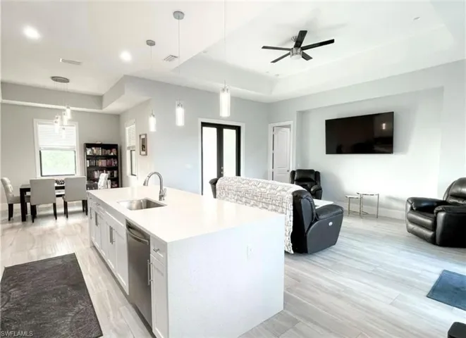 Kitchen featuring a tray ceiling, a sink, open floor plan, stainless steel dishwasher, and light wood-type flooring