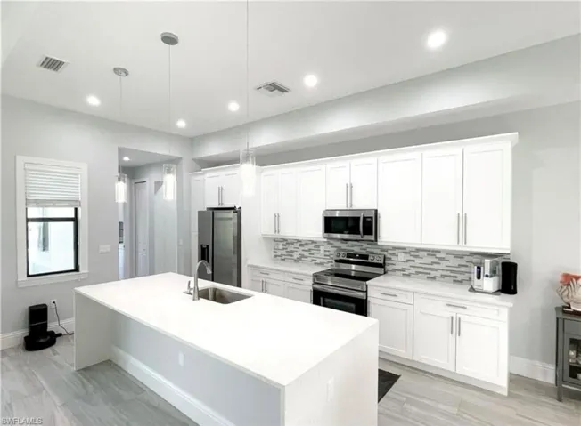 Kitchen with visible vents, a kitchen island with sink, a sink, decorative backsplash, and appliances with stainless steel finishes