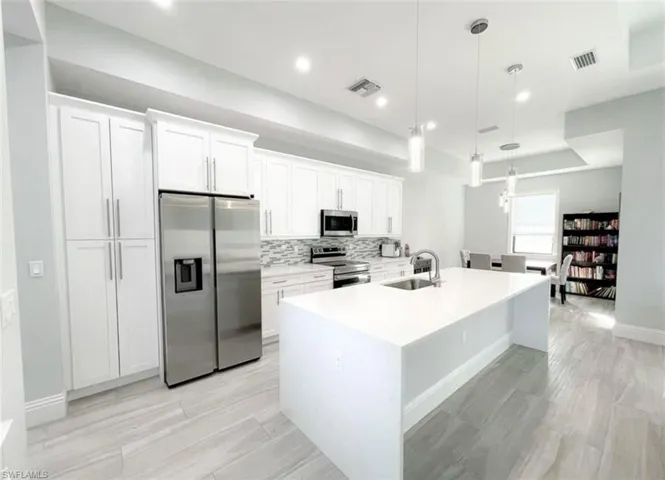 Kitchen featuring visible vents, a center island with sink, a sink, white cabinetry, and appliances with stainless steel finishes