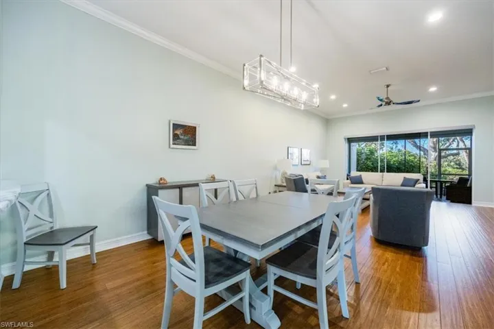 Dining room featuring hardwood floors, crown molding, ceiling fan and open concept with pass through from kitchen and views of lanai.