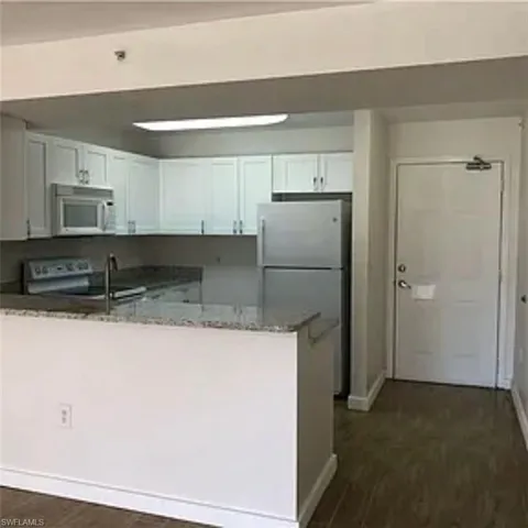 Kitchen featuring a peninsula, freestanding refrigerator, stone counters, white microwave, and dark wood-style flooring