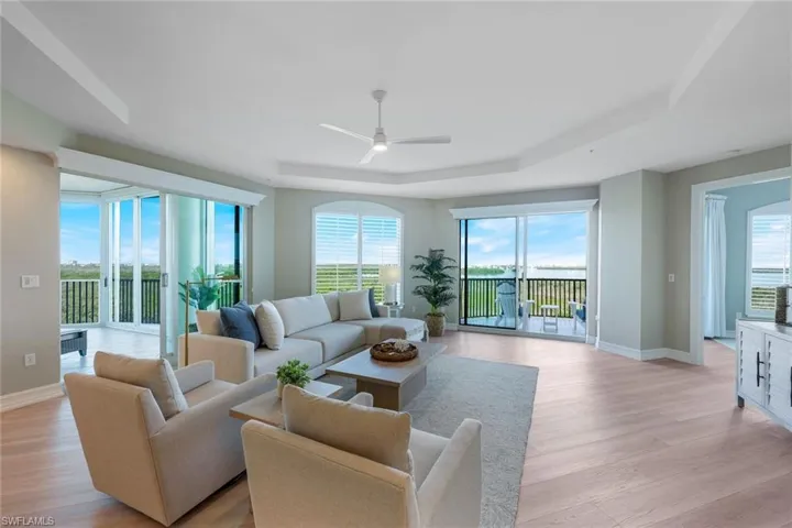 Living room featuring a tray ceiling, light wood-style floors, a ceiling fan, and plenty of natural light