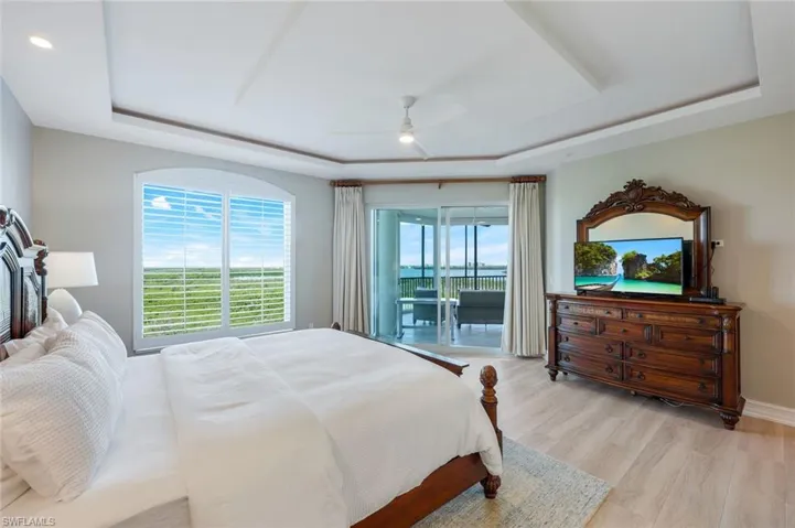 Bedroom with a tray ceiling, access to outside, light wood-style floors, ceiling fan, and baseboards