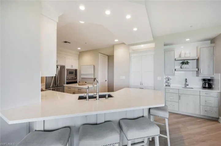 Kitchen featuring appliances with stainless steel finishes, a sink, open shelves, a breakfast bar, and recessed lighting