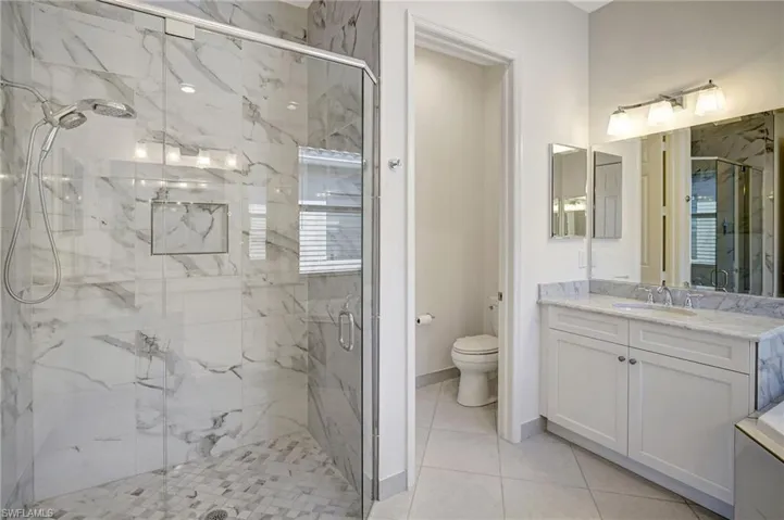 Bathroom featuring toilet, a marble finish shower, and vanity